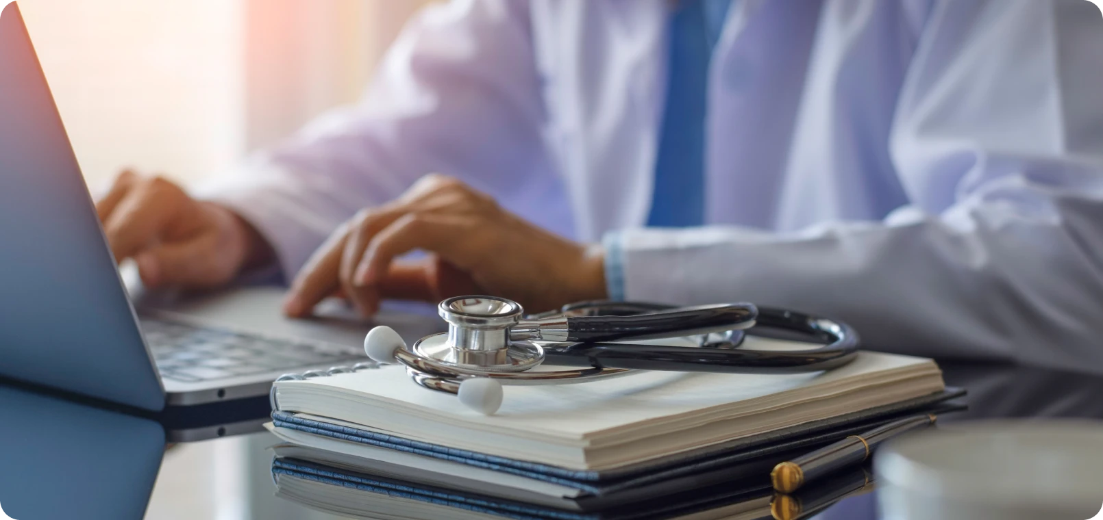 Healthcare worker writing on laptop with stethoscope
